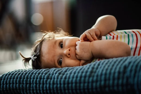 Adorable baby girl with fingers in mouth lying down on the pillow at home.