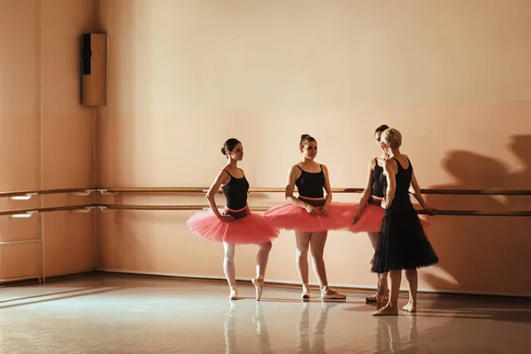 Group of female ballet dancers communicating with ballet instructor during a class at dance studio. Copy space.
