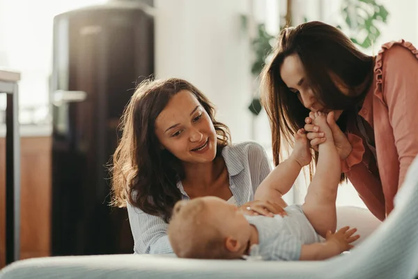 Two Young Women Enjoying Baby Son While One Them Kissing — Stok fotoğraf