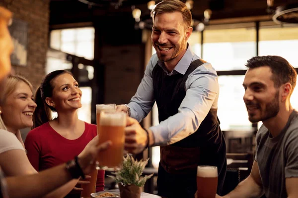 Happy waiter giving beer to his customers while serving them in a bar.