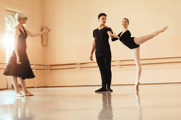 Ballet couple dancing with assistance of their instructor during ballet class in a studio.