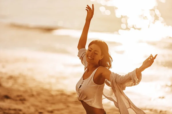 Carefree woman with arms outstretched having fun at summer sunset.