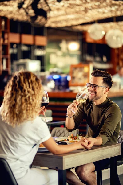 Happy couple having fun and drinking wine while holding hands in a restaurant.