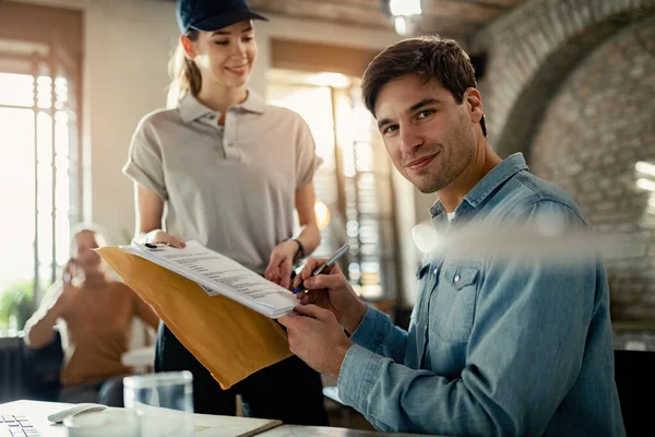 Young Businessman Signing Delivery Courier Office While Looking Camera — Stockfoto