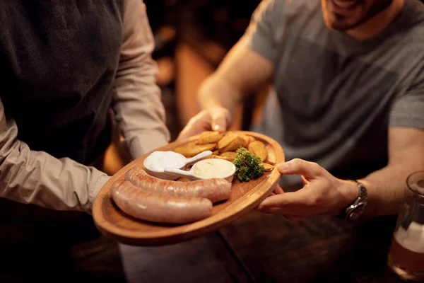 Close up of waitress serving sausages and potato to a guest during lunch time in a pub.