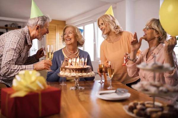 Happy senior people surprising their friend with a cake on Birthday party at home.