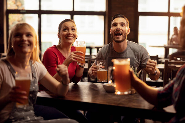 Group of happy young people drinking beer and watching sports match on TV in a pub. 