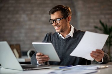 Happy businessman using touchpad and laptop while working on business reports in the office. 