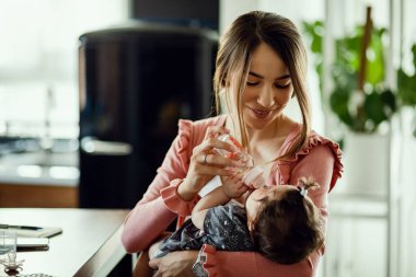 Young happy mother using baby bottle and giving water to her baby girl. 