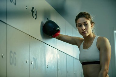 Low angle view of thoughtful sportswoman with boxing gloves trying to motivate herself before sports training. 