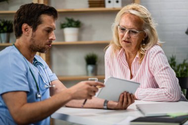 Mature woman and her doctor reading the results of medical analysis on touchpad at doctor's office. 