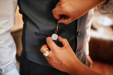 Close up of woman helping man to get ready on his wedding day and putting pocket watch in his waistcoat.  