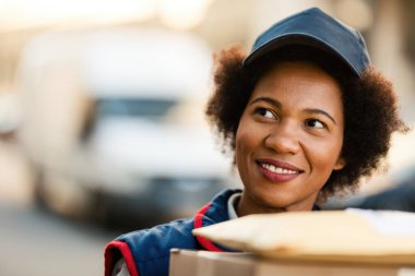 Smiling black mailwoman making a delivery in the city. 