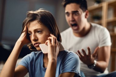 Sad woman thinking of something and ignoring her angry boyfriend who is yelling at her. 