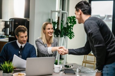 Two financial advisors having a meeting with young man at home. Female advisor is shaking hands with a client. 