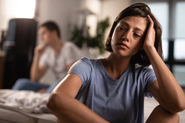 Unhappy woman contemplating after an argument with her boyfriend at home. The man is in the background.