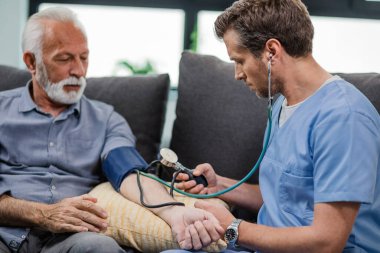 Doctor measuring blood pressure of a senior man while being in a home visit. 