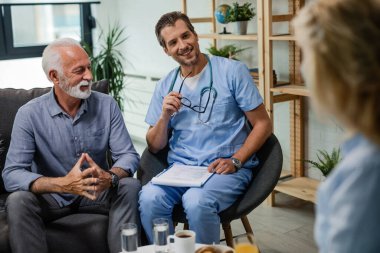 Happy general practitioner communicating with senior patients during a home visit. 