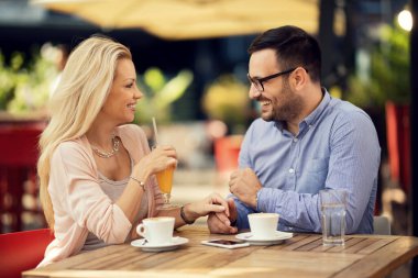Smiling couple holding hands and talking to each other while having a date in a cafe. 