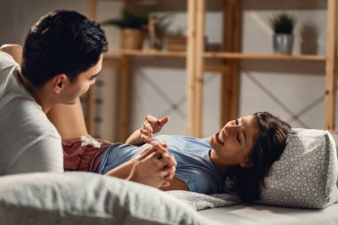 Young couple having fun while lying down in bedroom and communicating. Focus is on woman. 