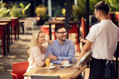 Happy couple enjoying in a cafe while talking to a waiter. 