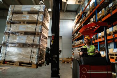 Manual worker using forklift while loading pallets in distribution warehouse. 