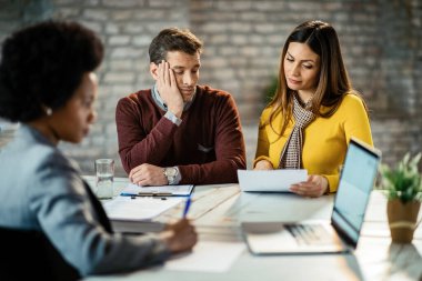 Mid adult couple going through paperwork and reading reports on a meeting with their financial advisor. Man is feeling bored. 