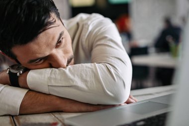 Exhausted businessman leaning on his desk and reading an e-mail on laptop in the office. 