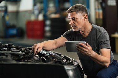 Auto repairman using touchpad while examining car engine in a workshop. 