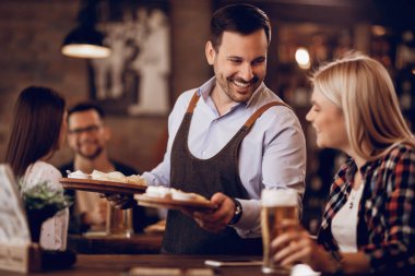 Happy waiter talking to a female customer while serving her food in a pub. 