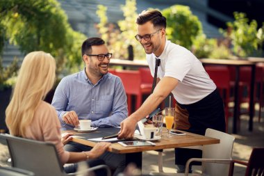 Smiling waiter serving guests in a restaurant and preparing their table for dining. 