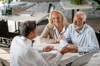 Mature couple communicating with financial advisor who is using digital tablet during consultations in the office. 