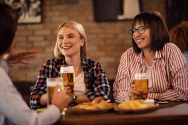 Young happy women talking to each other while drinking beer and relaxing in a bar. 