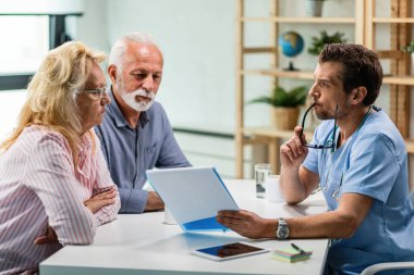 Concerned doctor explaining medical test results to mature couple while going through their documents.