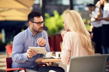 Mid adult man using digital tablet and talking to his girlfriend on coffee break in a cafe. 