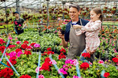 Happy father and daughter having fun while watering flowers with spray bottle at plant nursery. 