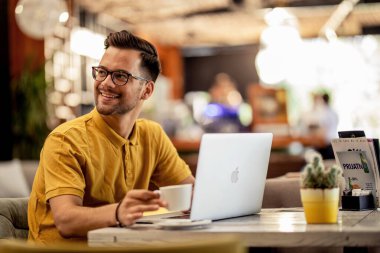 Happy male student using laptop while having coffee break in a cafe. 