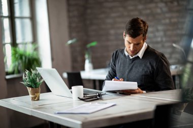 Businessman working in the office and taking notes while analyzing financial reports. 