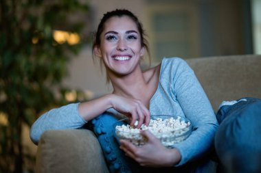 Young happy woman eating popcorn while enjoying in movie night at home. 