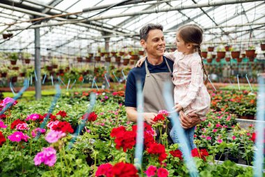 Happy father communicating with his daughter while taking care of flowers at plant nursery. 