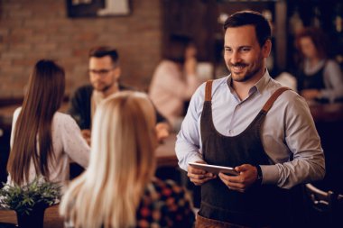Smiling man working part-time as a waiter and taking order from female guest in a bar. 