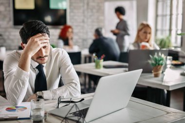 Pensive businessman holding his head in pain while reading problematic e-mail on the computer at work 