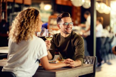 Young loving couple holding hands and drinking wine while eating in a restaurant. 