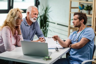 Senior couple talking with their doctor while he is showing them something on a computer. 