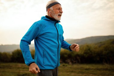 Mature athletic man getting out of breath while jogging in the morning in nature. 