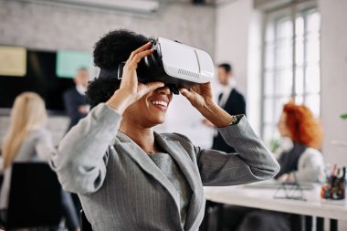 Happy black businesswoman having fun while wearing VR glasses in the office. 