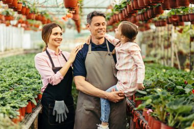 Happy family communicating while working in their greenhouse. Father is holding little girl in his arms. 