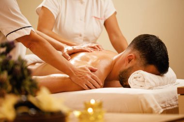 Two unrecognizable therapists massaging back of a man at health spa. 