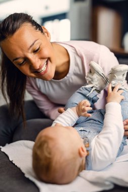 Young mother having fun with her baby boy while playing with him of the sofa at home. 