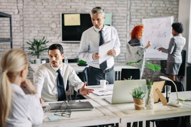 Small business team talking to each other at work in modern office. Focus is o mid adult businessman. 
